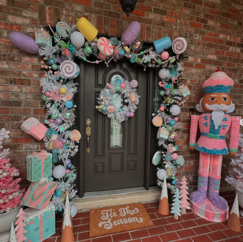 A front door styled as a whimsical candy land with pastel garland, oversized candy props, gift boxes, and a colorful nutcracker